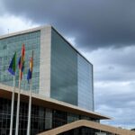 Bandeira arco-íris desbotada em poste de rua em Brasília, com Congresso Nacional ao fundo, simbolizando vulnerabilidades da população LGBTQIAPN+ no DF.