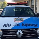 Viatura da Polícia Federal em frente a prédio oficial no Rio de Janeiro, com Pão de Açúcar ao fundo.