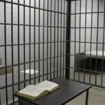 Cela de prisão brasileira com Bíblia e cruz, sem Smart TV, em estilo fotojornalístico.