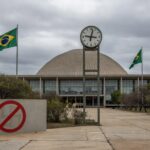 Edifício da CLDF em Brasília com relógio atrasado e símbolos anti-nazistas, representando audiência pública para lei contra propaganda nazista amid críticas por atrasos.