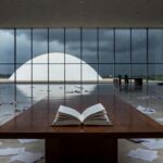 Edifício da CLDF em Brasília com livro sobre mesa em salão vazio, simbolizando lançamento em meio a crises e controvérsias.