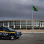 Edifício da CLDF em Brasília com símbolos de combate à violência contra a mulher e viatura policial, destacando falhas na reintegração de policiais.