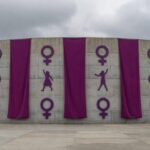 Edifício da CLDF em Brasília decorado com faixas roxas para o 8 de Março, mascarando violência contra mulheres em desfile.