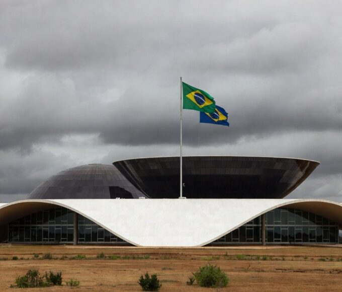 Fachada da Câmara Legislativa do DF com elementos simbólicos de cerimônia e pilhas de documentos, destacando críticas à lentidão judicial.