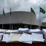 Edifício da Câmara Legislativa do DF em Brasília, com bandeiras e placas de homenagem, sob céu nublado, representando crises no Distrito Federal.