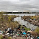 Área ambiental degradada no DF com lixo e vegetação poluída, ao fundo prédio da CLDF, destacando falhas persistentes em meio a homenagens.