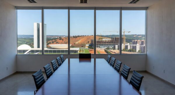 Sala de reuniões em Brasília com vista para edifícios de saúde e habitação, representando avanços governamentais.