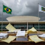 Edifício da CLDF em Brasília com bandeiras e documentos simbólicos de ônus financeiro público.