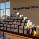 Pilhas de caixas de chocolate doadas pela Rede Dona para Páscoa solidária no DF, em ambiente comunitário de Brasília.