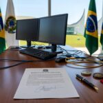Mesa com decreto de autonomia para licitações em tecnologia no governo do DF, com equipamentos tecnológicos e bandeiras oficiais.