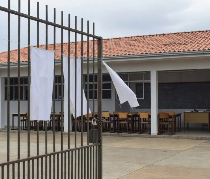 Escola pública em Brasília com portões fechados e faixas de greve, representando paralisação de professores no DF.